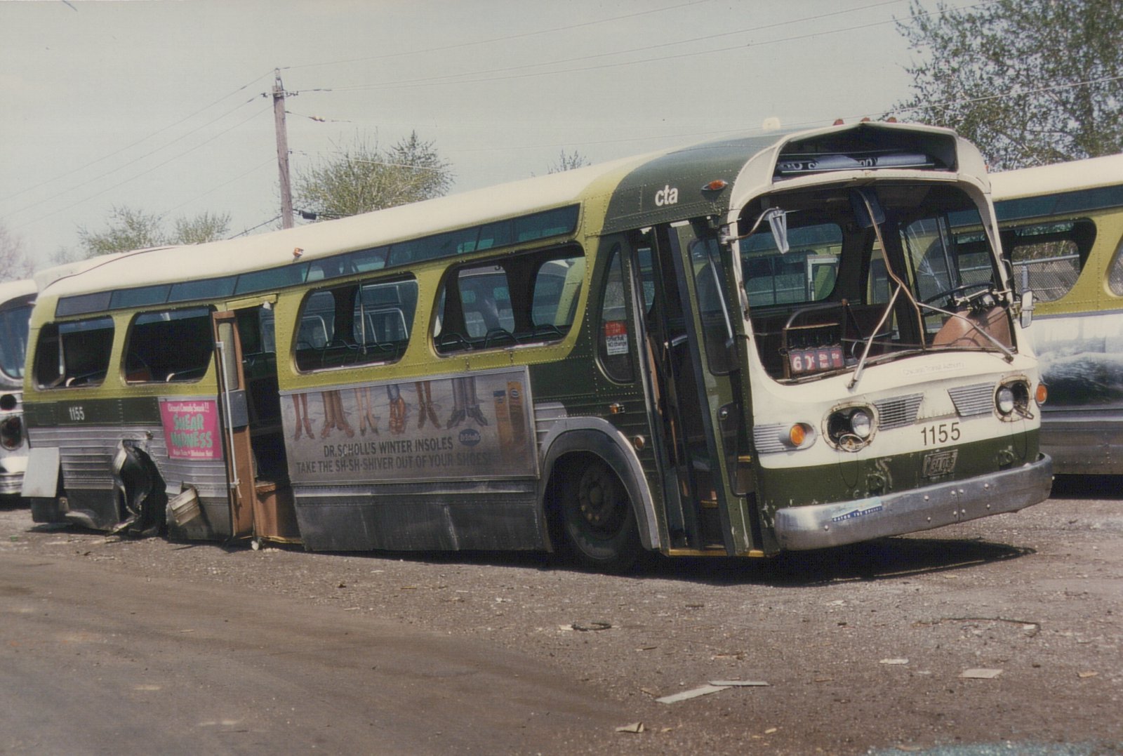 A green and cream CTA bus, number 1155, parked in a gravel yard with visible damage to its rear and side, showing a route 62 sign and advertisements.