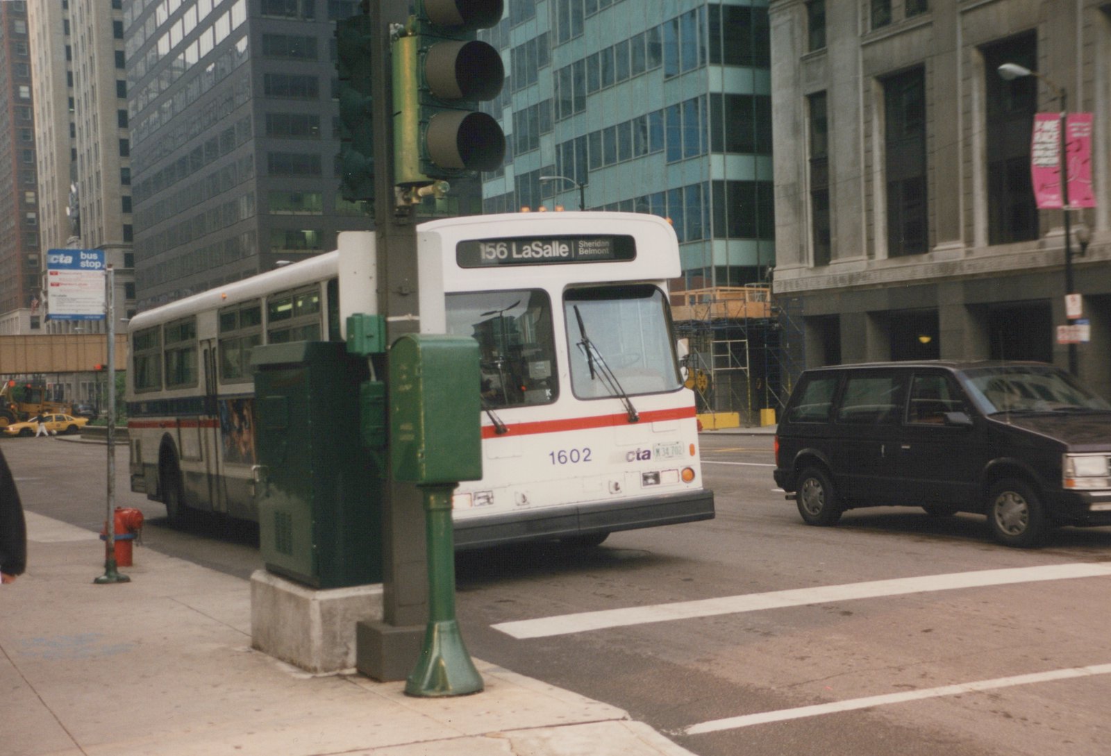 A white CTA bus with red and blue stripes, number 1602, on a city street with tall buildings in the background.