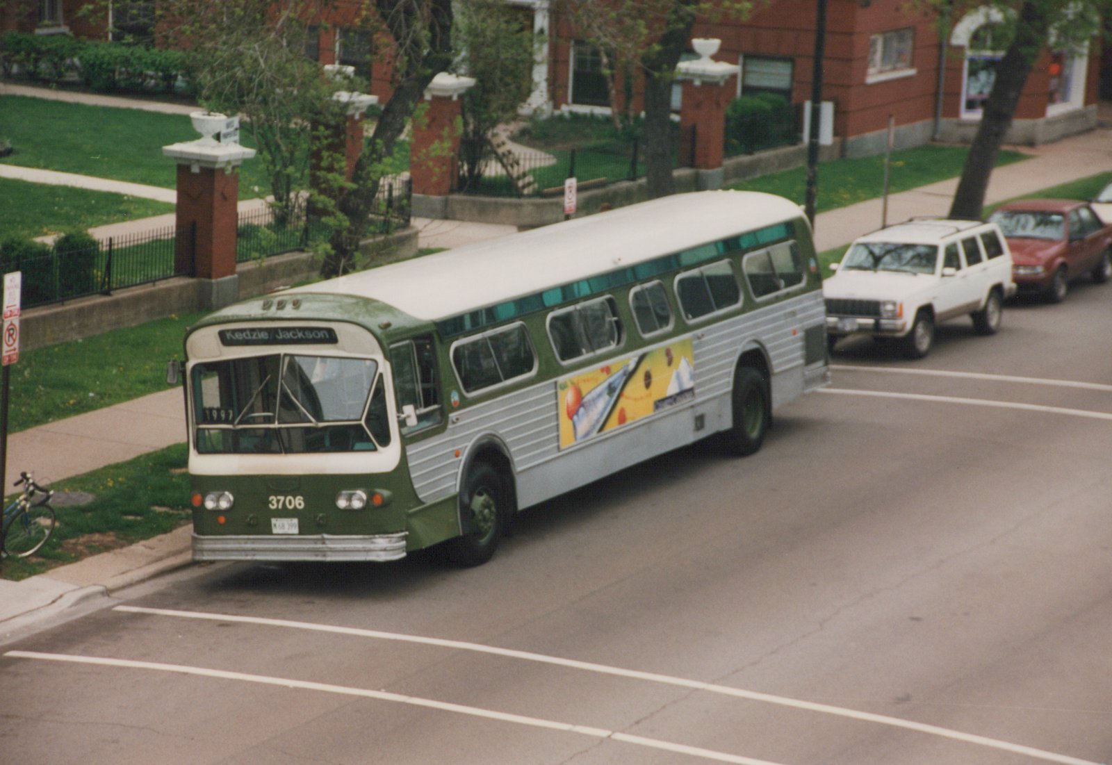 A green and cream Chicago Transit Authority bus with the number 3706 on its front is turning on a city street, with a 'Kedzie/Jackson' destination sign, surrounded by parked cars and a sidewalk with trees.