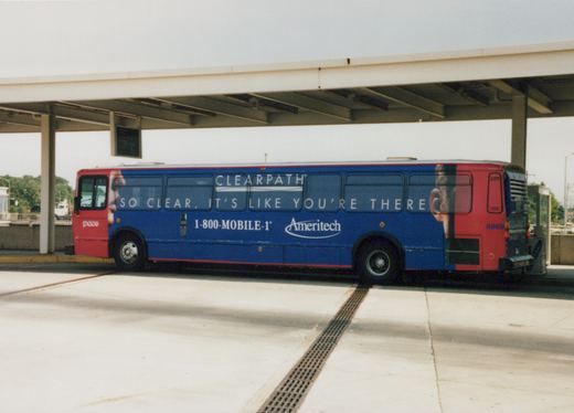 A blue and red Pace bus with number 8869 is parked sideways under a concrete shelter at a terminal, displaying a large Ameritech ad on its side.