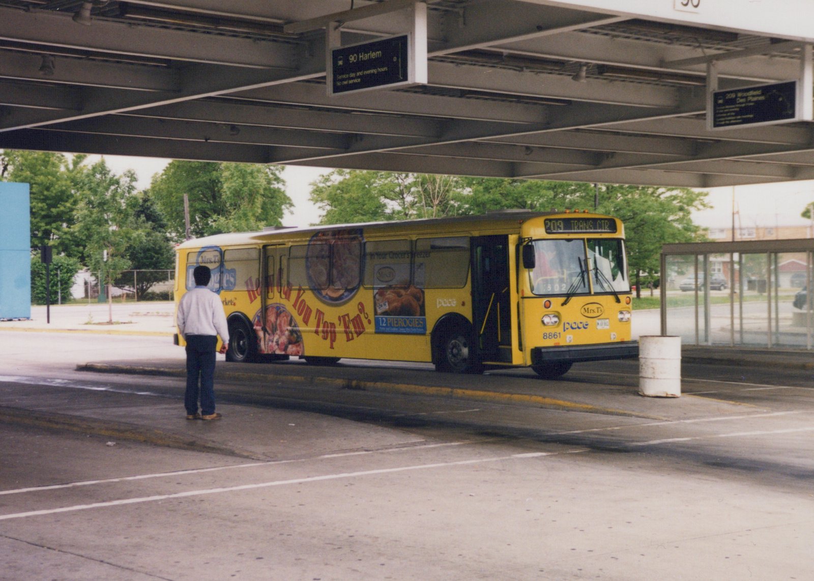 A yellow Pace bus numbered 8861 is parked at a terminal under an overhead structure, with a person standing nearby.