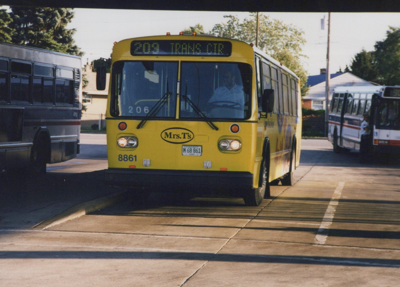 Front three-quarter view of a yellow Pace bus number 8861 with a Mrs. T's ad, showing route 209 to Trans Ctr, parked alongside other buses on a sunny day.