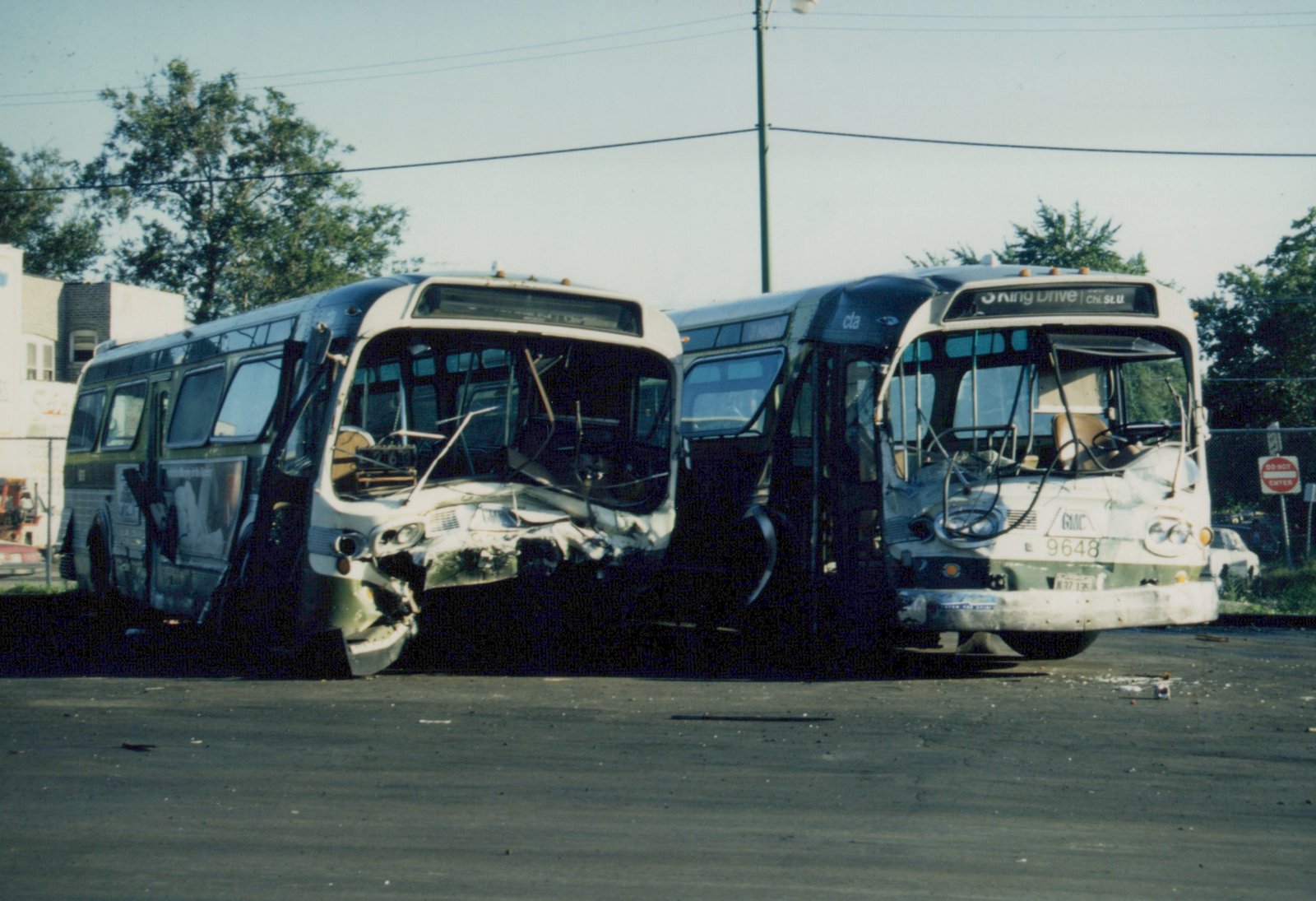 Two damaged CTA buses in a lot, one with a crushed front end and the other with a visible fleet number 9648 and destination sign reading '5 King Drive'.