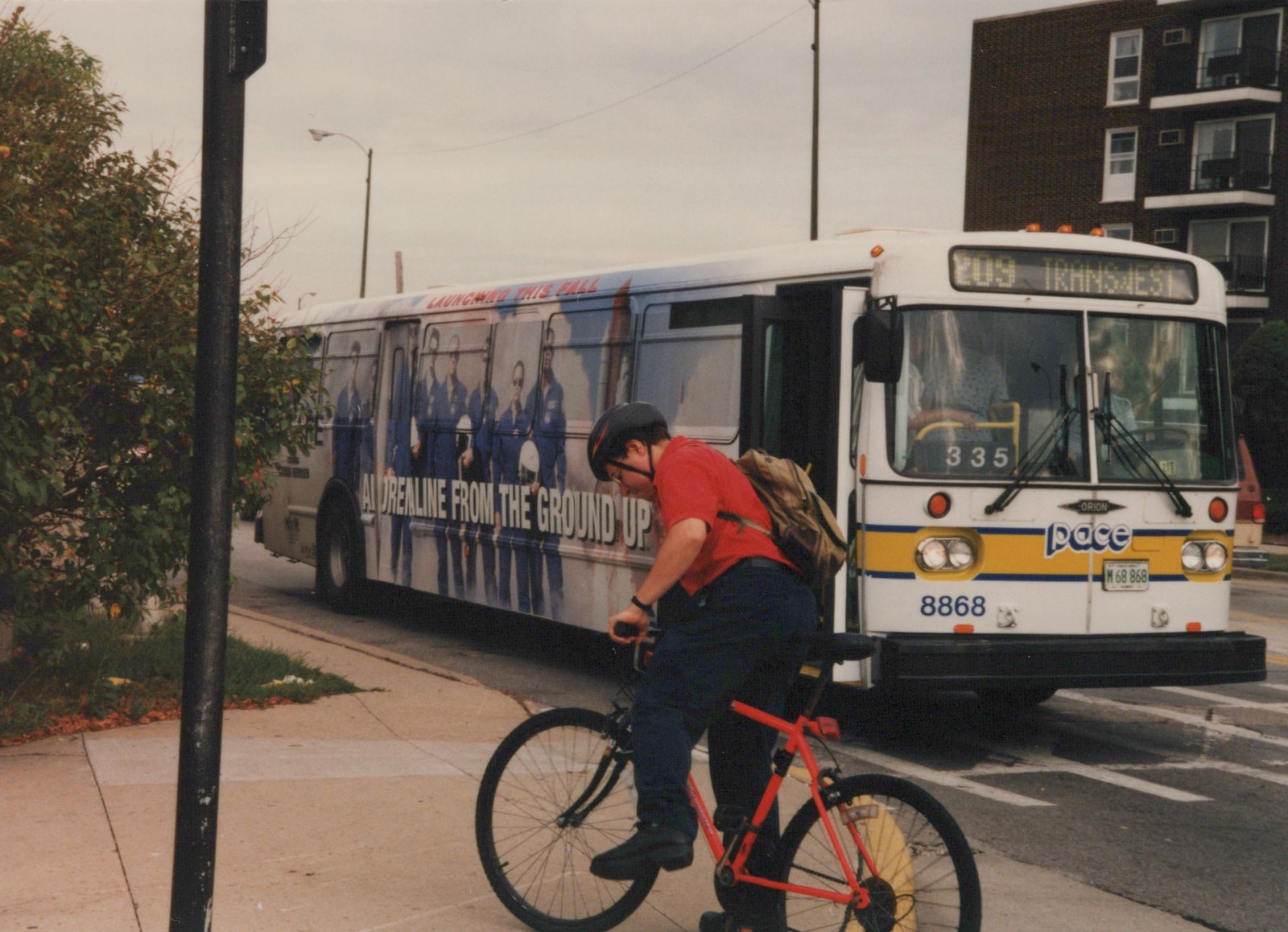 A white and yellow Pace bus with the number 8868 is stopped on a city street, with a cyclist on a red bicycle riding on the sidewalk in front of it.