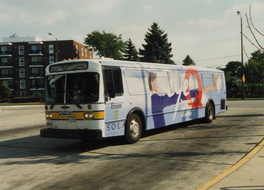 A white Pace bus with a large 'Eye Q' ad on its side is parked on a street with trees and buildings in the background.