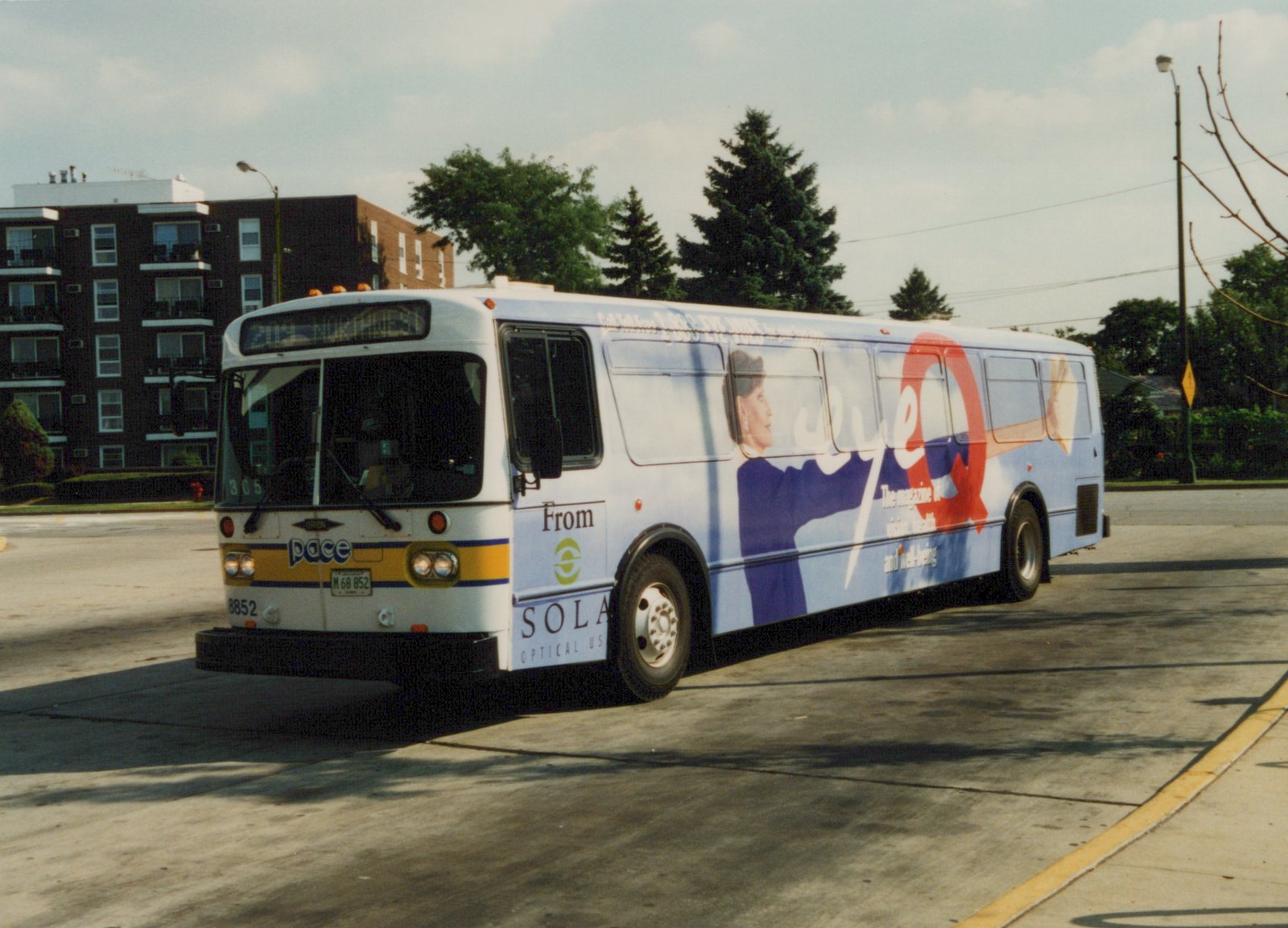 A white Pace bus with a large 'Eye Q' ad on its side is parked on a street with trees and buildings in the background.