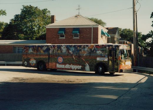 A Pace bus with a full-wrap Chicago Cubs advertisement is parked on a quiet street, showing the side and front of the vehicle.