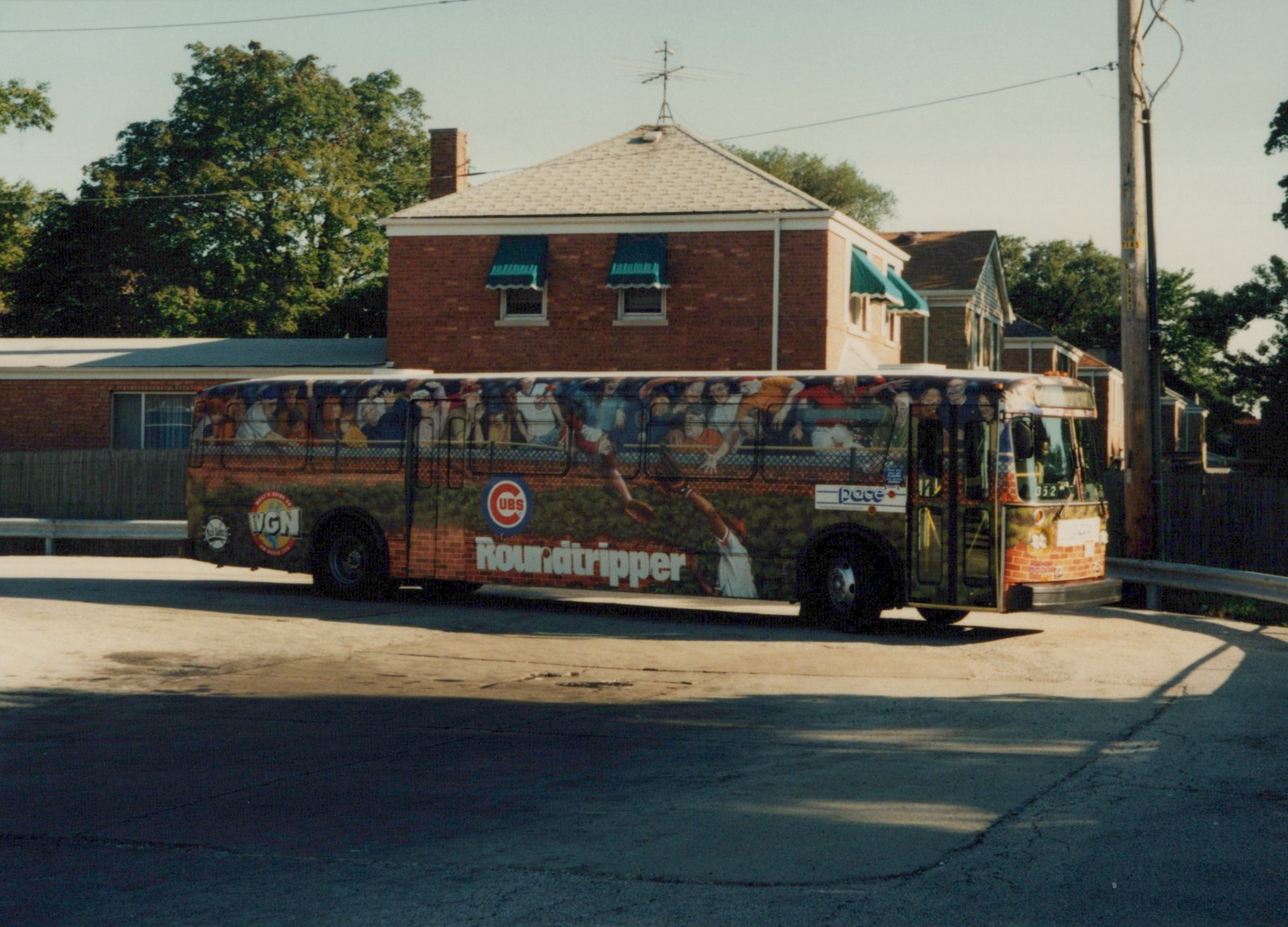 A Pace bus with a full-wrap Chicago Cubs advertisement is parked on a quiet street, showing the side and front of the vehicle.