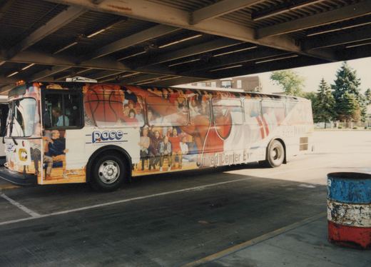 A white Pace Motor bus with a colorful basketball-themed wrap and 'United Center Express' lettering is parked under a bridge on a sunny day, with two people visible inside.