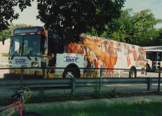 A white PACE bus with a colorful advertising wrap reading 'United Center Express' is parked behind a fence with trees and green grass in the foreground.