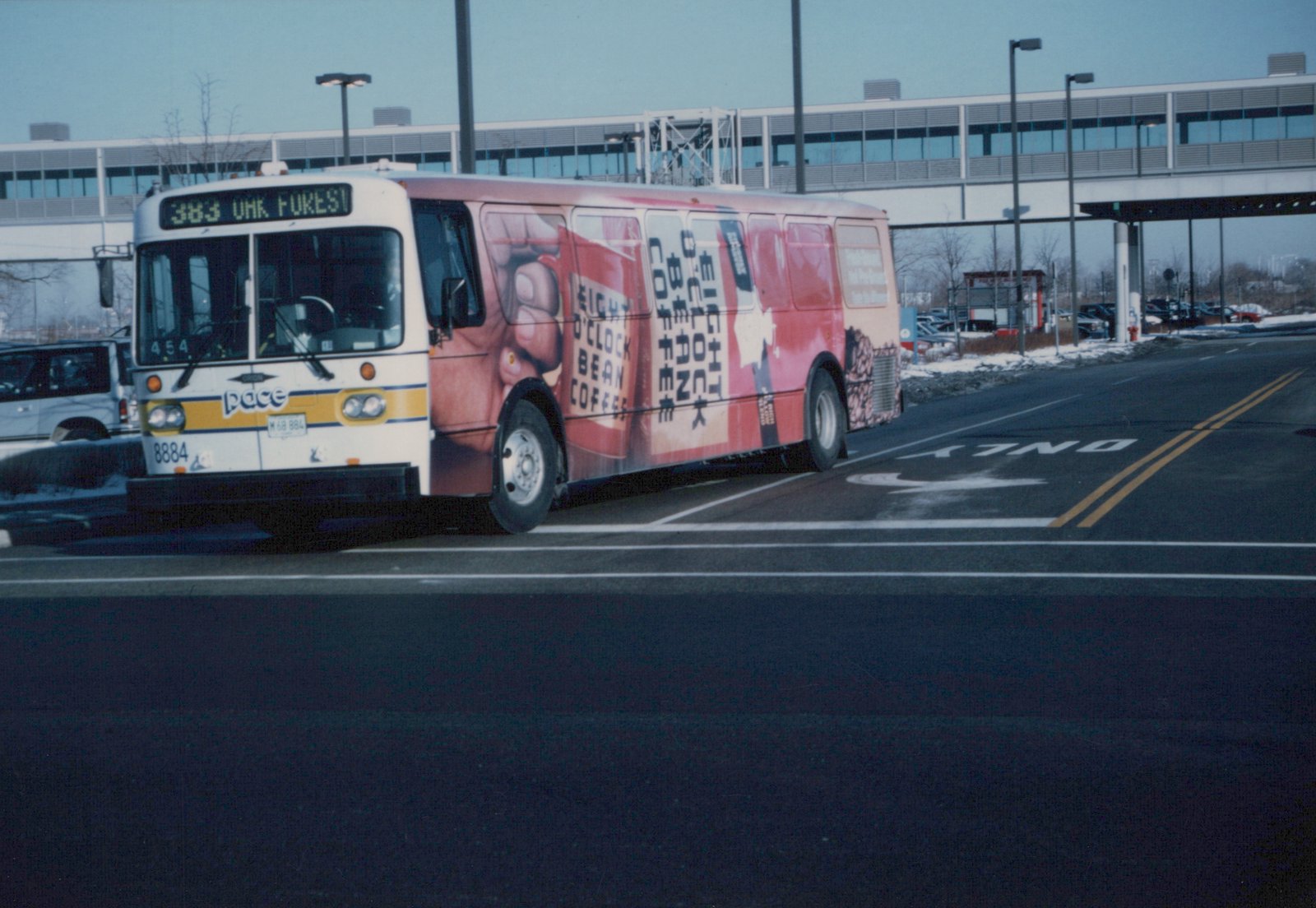A white Pace bus with a red advertisement wrap is parked on a snow-lined street, showing its front and side in daylight.