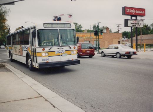 A white Pace bus, number 8866, turns at a street corner on an overcast day, with a Walgreens sign and other vehicles in the background.