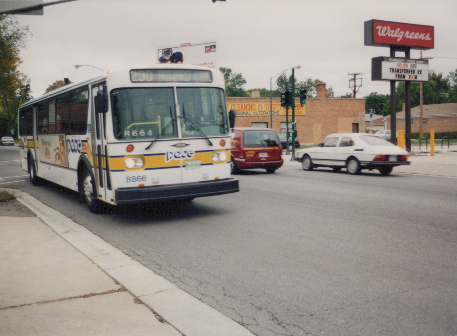 A white Pace bus, number 8866, turns at a street corner on an overcast day, with a Walgreens sign and other vehicles in the background.