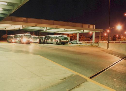 Several CTA buses parked at a covered terminal at night, with people boarding and a car parked nearby.