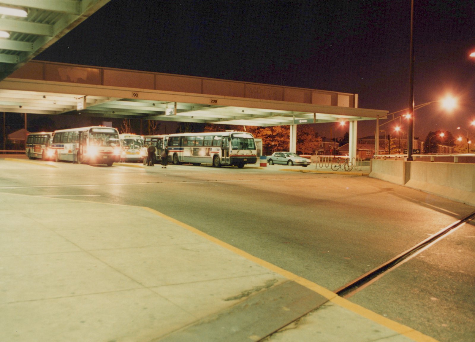 Several CTA buses parked at a covered terminal at night, with people boarding and a car parked nearby.