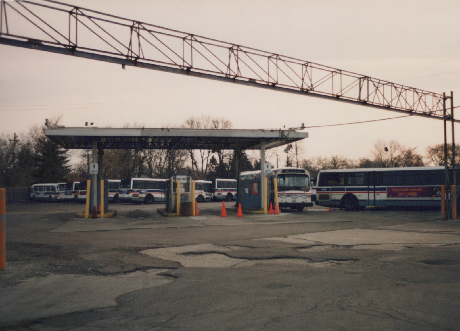 Several Chicago Transit Authority buses, including numbers 9293 and 5406, are parked at a gateway inside a bus garage, with bare trees in the background.