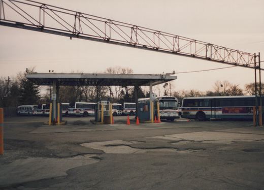 Several Chicago Transit Authority buses, including numbers 9293 and 5406, are parked at a gateway inside a bus garage, with bare trees in the background.