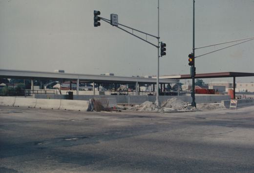 A construction site with concrete barriers, a pile of dirt, and traffic lights under an overpass being built.