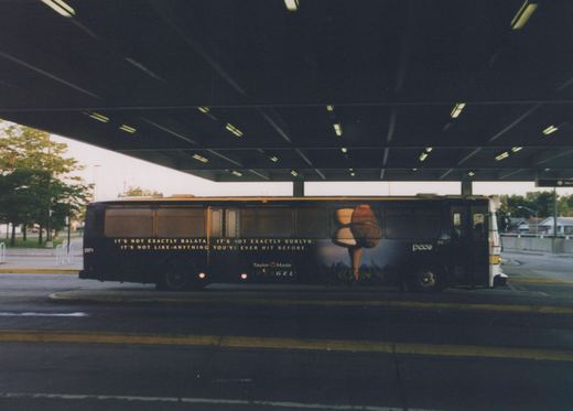 A dark blue Pace bus, number 2371, is parked under the roof of a terminal. An advertisement for Taylor Made INKEGEL golf balls covers its side.