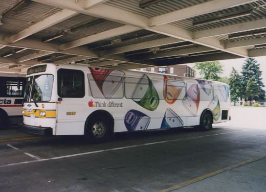 A white Pace bus with the number 8857 and an Apple 'Think different' ad is parked under an overpass. Another bus is partially visible in the background.
