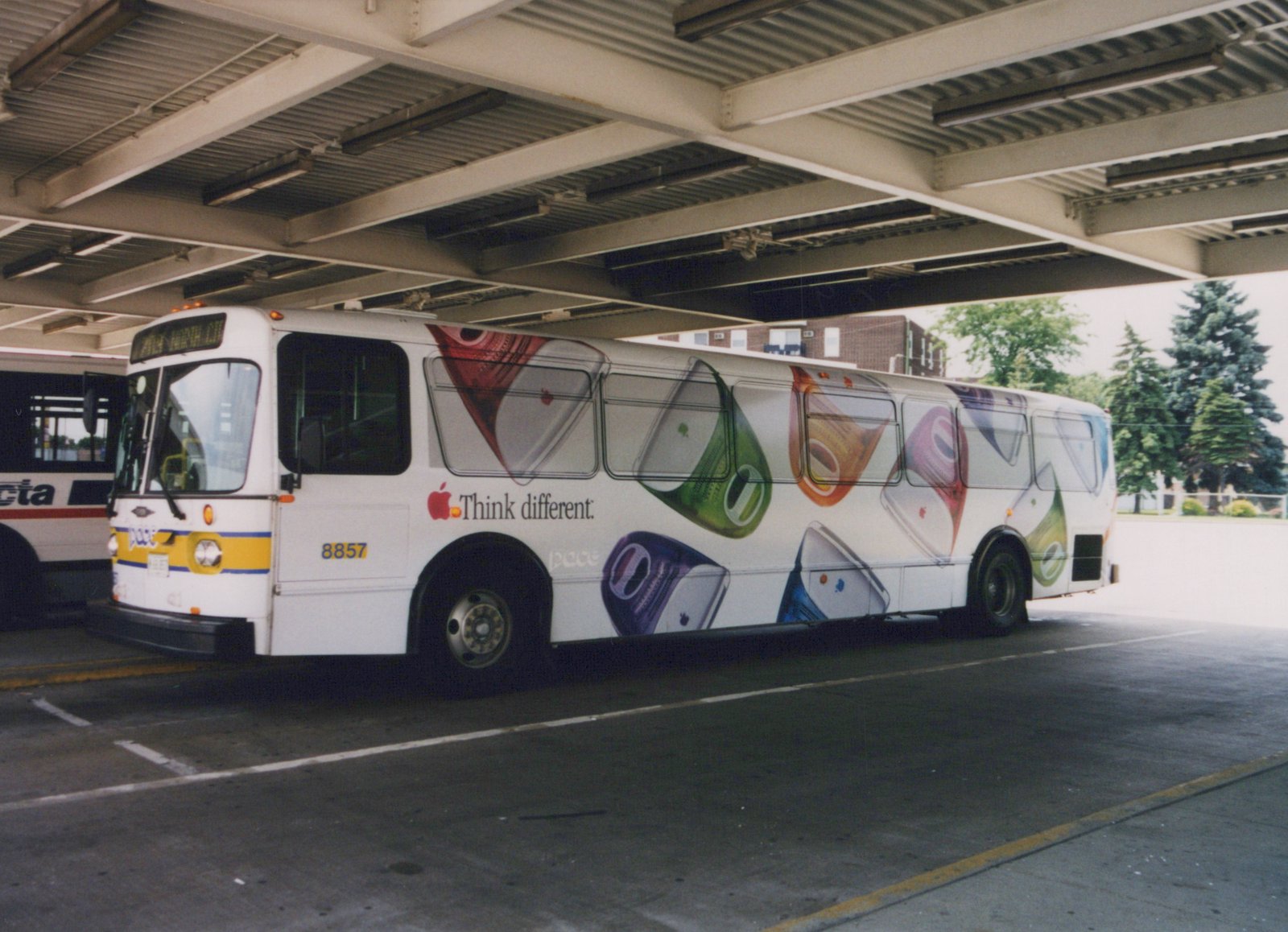 A white Pace bus with the number 8857 and an Apple 'Think different' ad is parked under an overpass. Another bus is partially visible in the background.