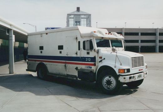 A white Chicago Transit Authority Grumman motor bus, numbered 312, parked at an outdoor transit facility with a multi-story parking garage in the background.