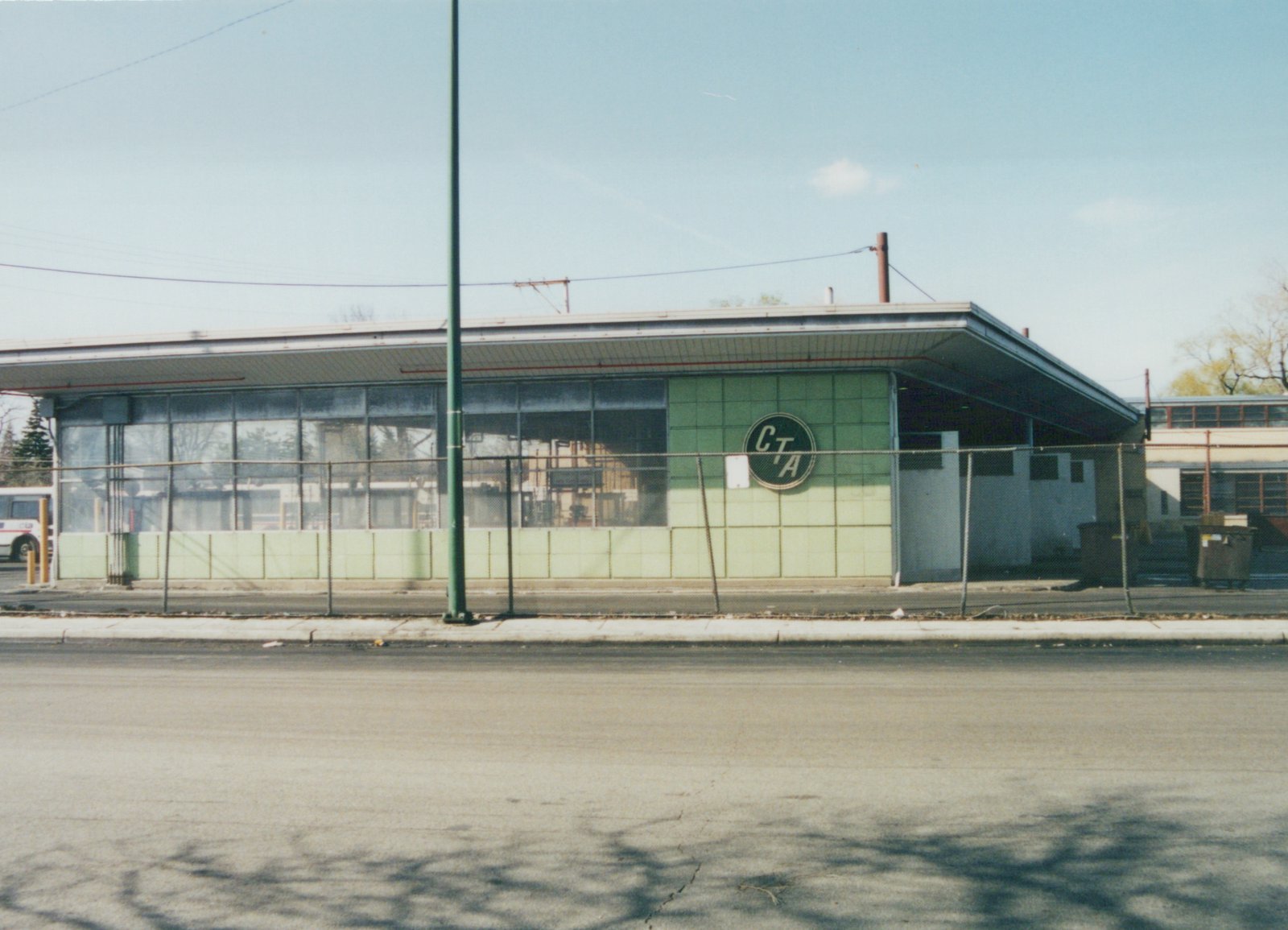 A street-level view of the Chicago Transit Authority's Forest Glen Garage, a mid-century modern building with a green tile exterior and a large circular CTA logo, with a bus visible inside through the windows.