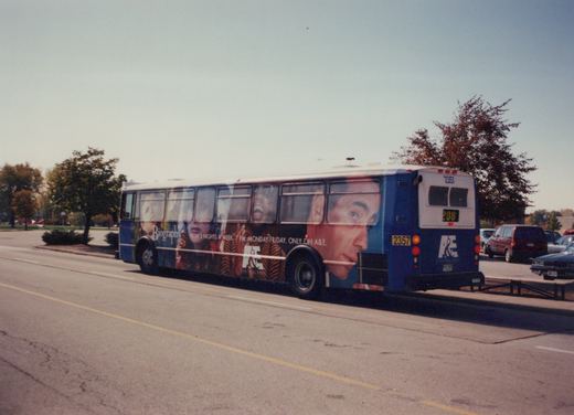 A blue and white Pace bus with the number 2357 and a large Biography channel ad on its side, parked on a street with trees and other cars in the background.