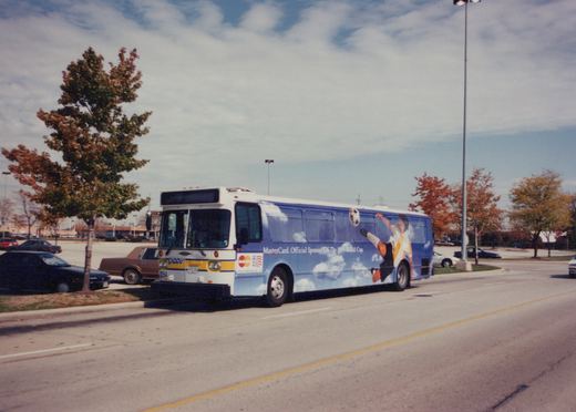A white and blue Pace motor bus with the number 2354 on the front is parked on a street lined with autumn trees. The side of the bus features a large advertisement for the 1994 World Cup sponsored by MasterCard.