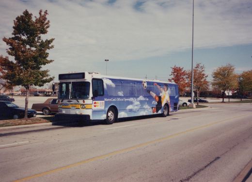 A white and blue Pace bus, numbered 2354, is parked on a street with autumn trees and a clear sky, featuring a large MasterCard World Cup ad on its side.