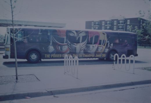 A purple CTA bus with a Power Rangers movie ad on its side, parked at a curb next to a bike rack and a young tree, with an apartment building in the background.