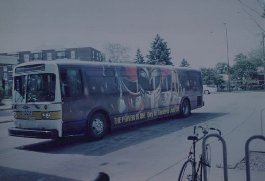 A white and blue Pace motor bus, number 8852, is parked on a street with a 'Power Rangers' movie ad on its side. A bicycle is locked to a rack nearby.