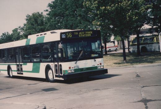 A white and green Chicago Transit Authority bus on route 56 to Jeff Park Station, parked on a paved lot with trees and another bus in the background.