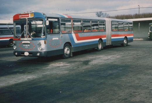 A silver articulated bus with red and blue stripes and red stars, labeled CTA and number 1976, parked in a paved yard under an overcast sky.