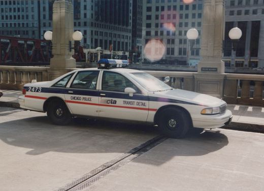 A white and blue Chicago Police CTA Transit Detail car, number 2473, is parked on a city bridge on a sunny day with tall buildings in the background.