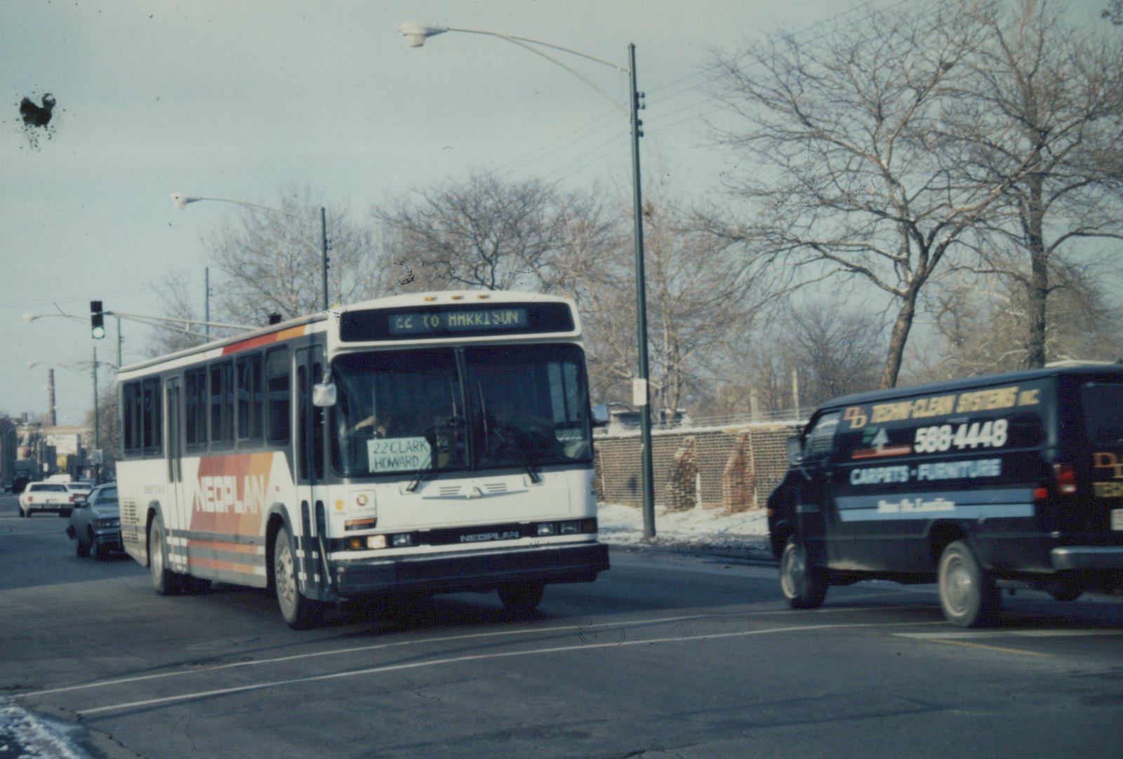 A white Neoplan bus on a city street with bare trees and snow, showing its destination as '22 TO HARRISON' and route as '22 CLARK HOWARD'.