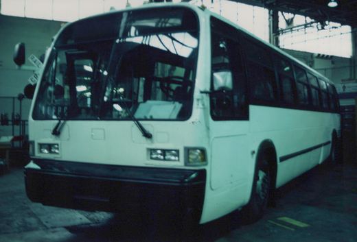 A white GM New Look TDH-5303 motor bus is parked inside a large bus garage, viewed from a three-quarter front angle.