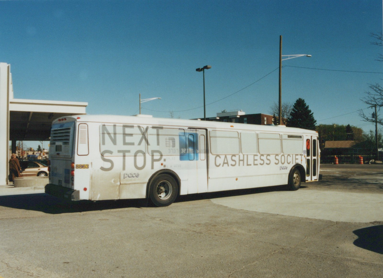 A white Pace bus with fleet number 8863 is parked on a paved lot, its side displaying a large American Express advertisement that reads 'NEXT STOP: CASHLESS SOCIETY'.