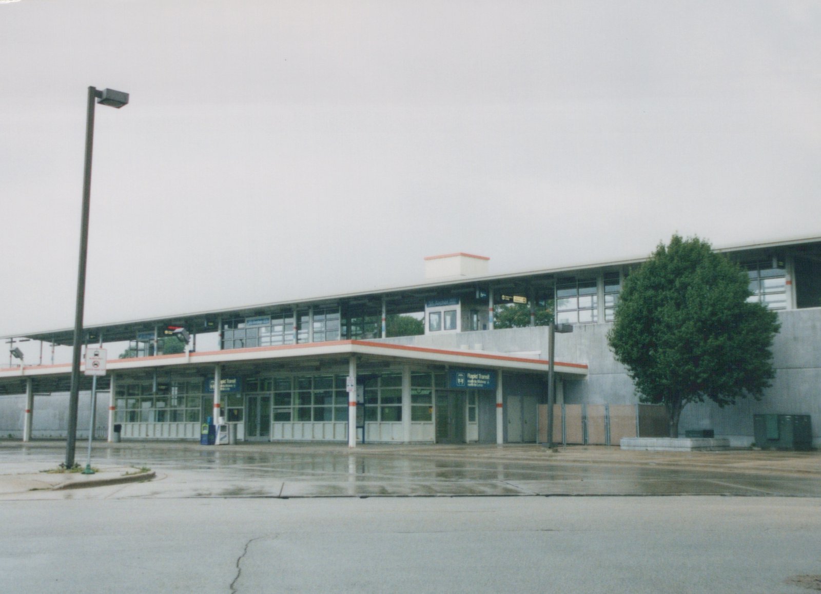 An empty, modern-looking elevated train station with a concrete building and a sign that reads '35 Archer Ave' under a gray sky.