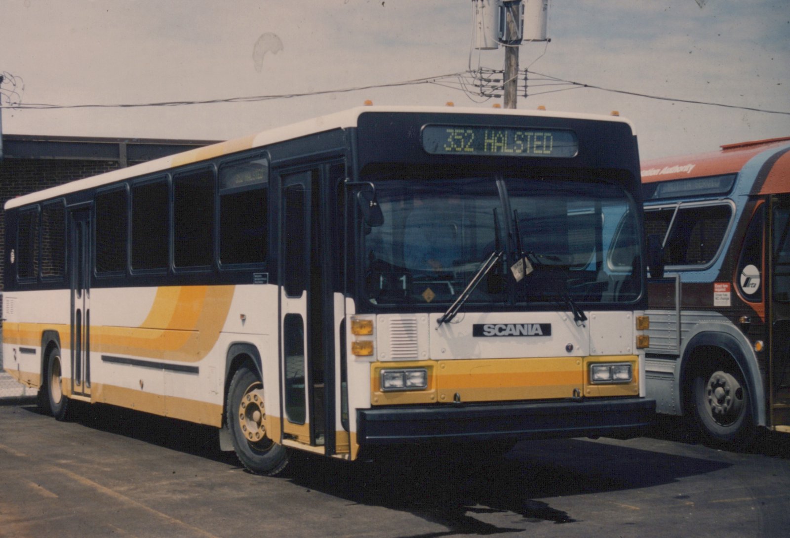 A white and yellow Pace South Division Scania bus, numbered 352 and showing 'HALSTED' on its destination sign, is parked on a street with another bus partially visible behind it.