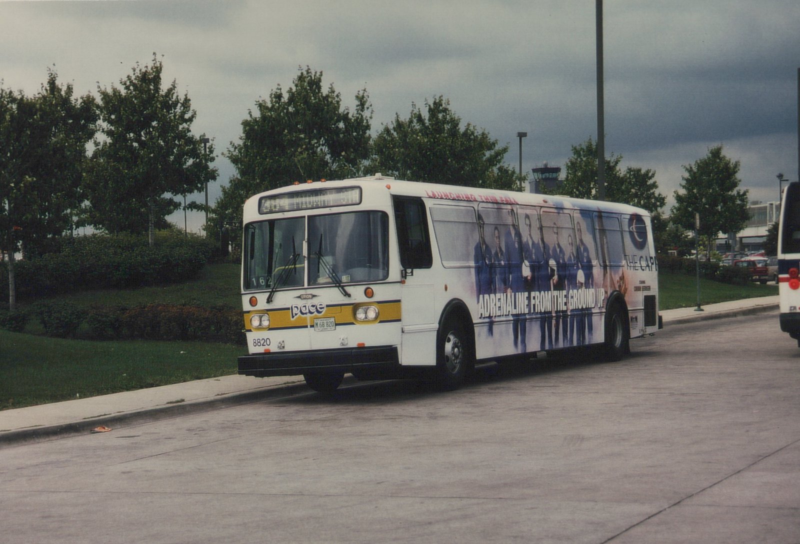 A white Pace Orion V bus with fleet number 8820 is parked on a street, displaying a side advertisement and an overcast sky in the background.