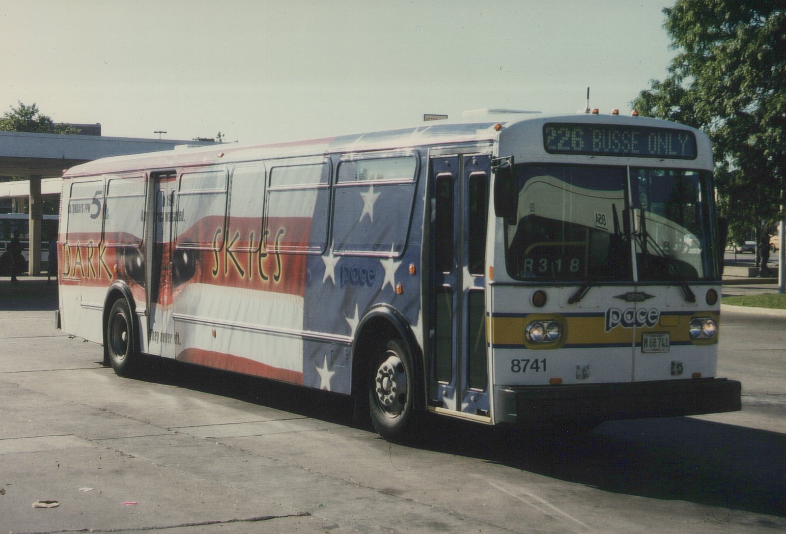 A white Pace bus with a patriotic 'Dark Skies' movie ad on its side, showing route 226 to Busse, parked outdoors on a sunny day.
