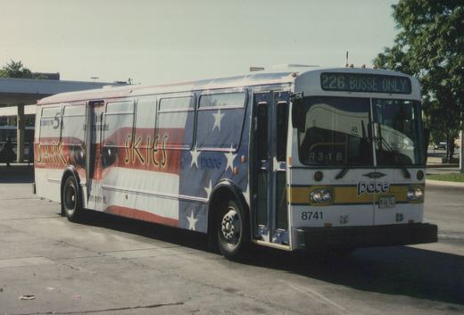 A white Pace bus with a patriotic 'Dark Skies' movie ad on its side, showing route 226 to Busse, parked outdoors on a sunny day.