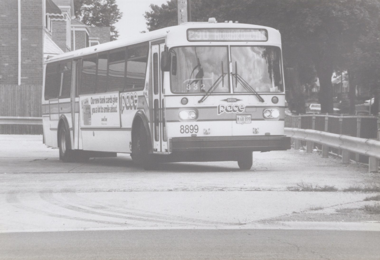 A front three-quarter view of a white Pace bus with the number 8899, parked on a street with a guardrail and trees in the background.