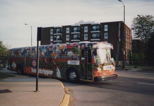 A city bus with a full wrap showing baseball players and the Chicago Cubs logo is parked on a street. The bus is marked with the operator name 'Pace' and the number 8858 on the front bumper. A brick apartment building is in the background.