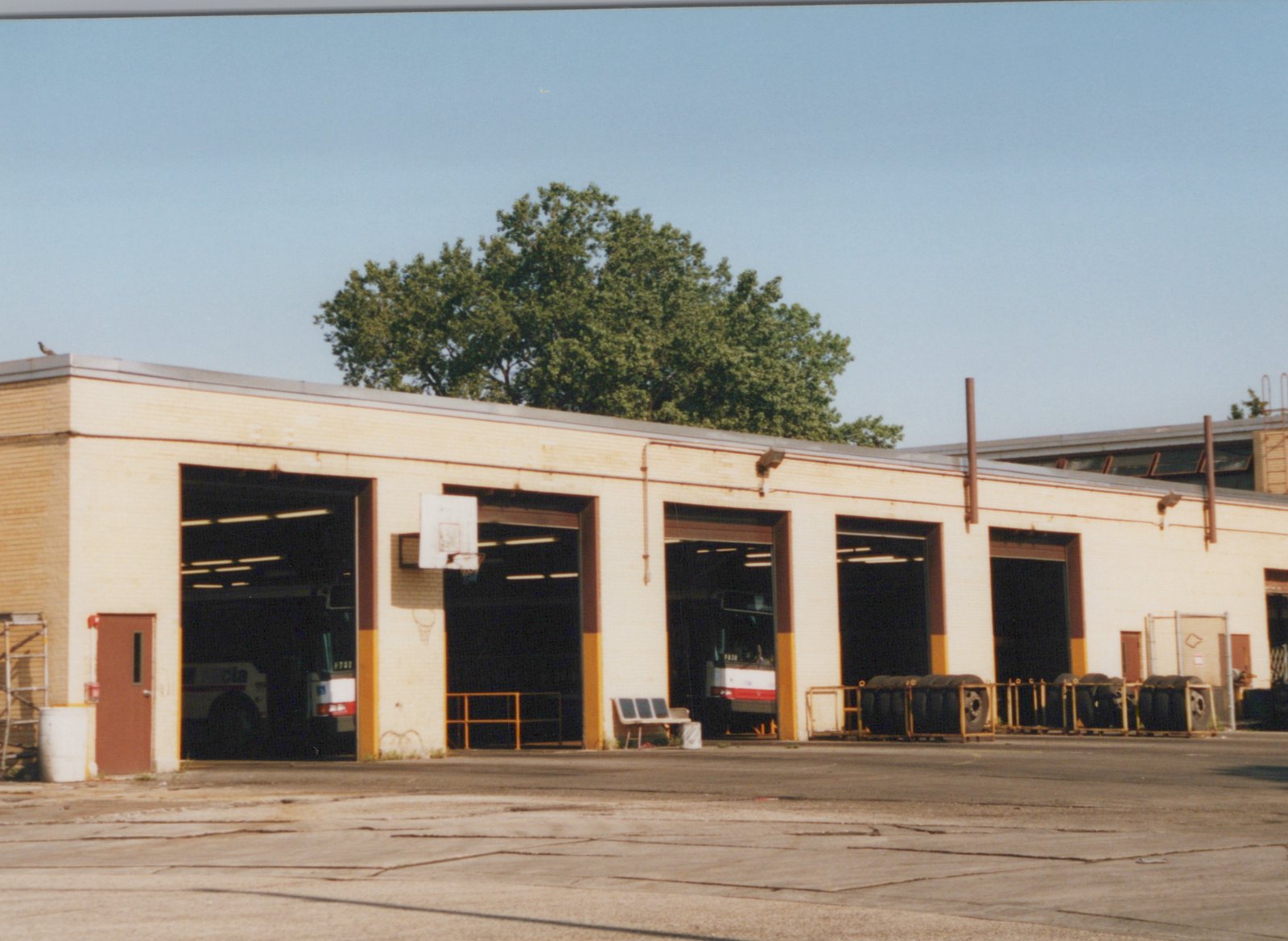 Exterior view of a brick bus garage with multiple open bays revealing buses inside, marked with CTA livery and numbers 782 and 780, set against a clear blue sky.