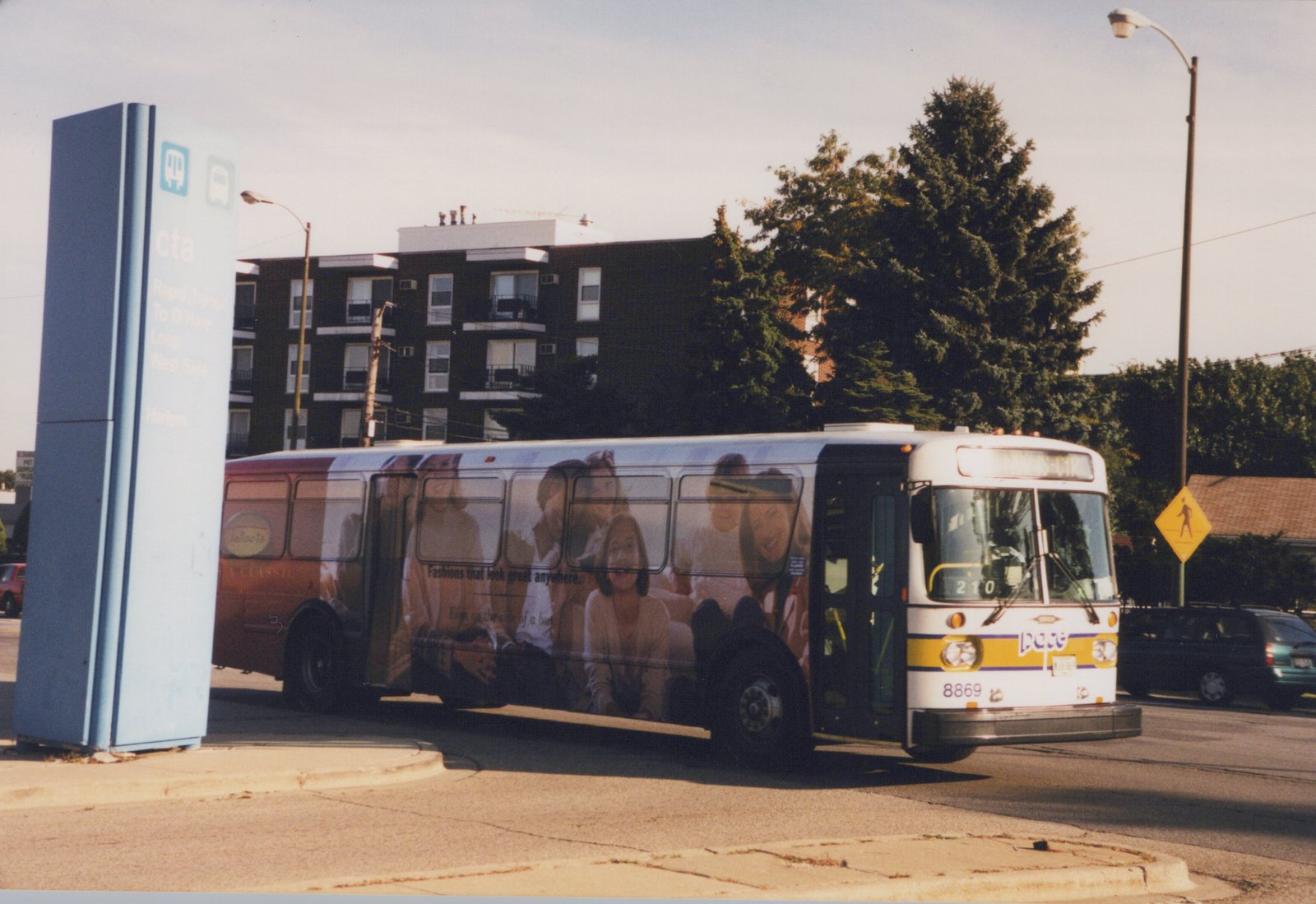 A white Pace bus with fleet number 8869 is parked on a city street next to a blue CTA sign that reads 'Harlem'.