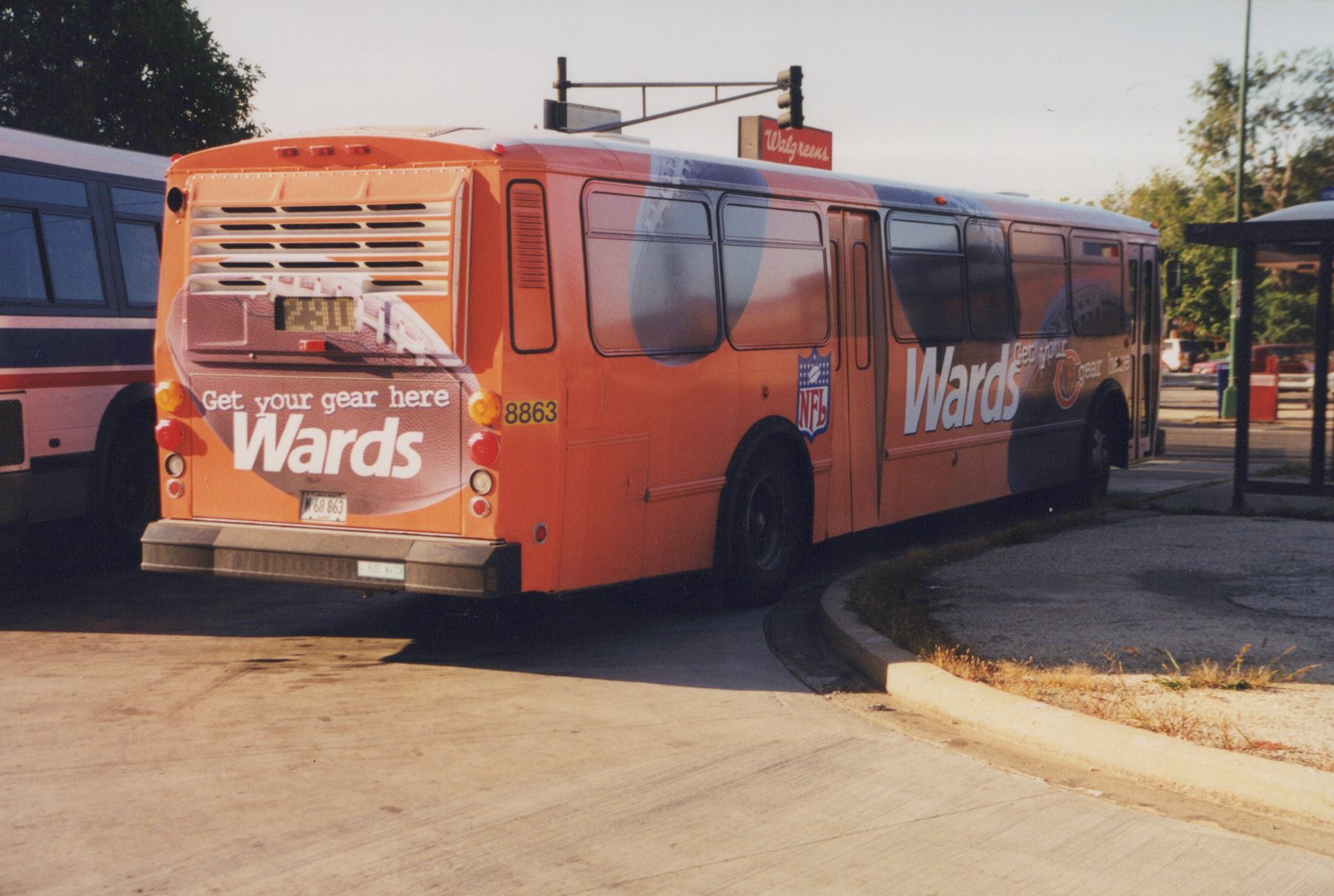 An orange Pace bus with the number 8863 on its rear and side, featuring a Wards and NFL advertisement, parked on a sunny street.