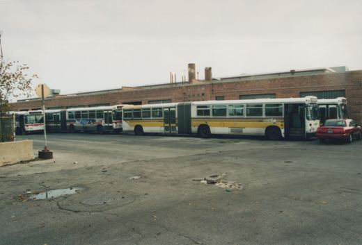 Several articulated buses from the Chicago Transit Authority are parked side-by-side in an asphalt lot in front of a brick building on an overcast autumn day.