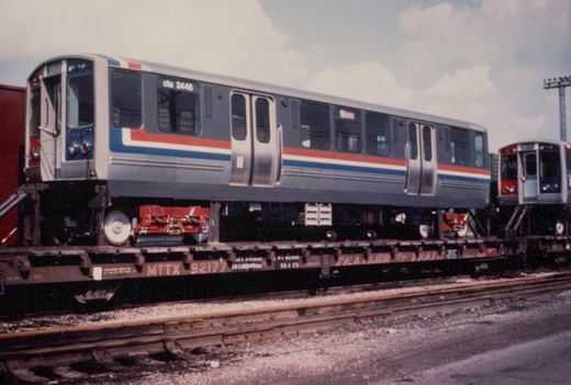 A side view of a silver CTA 2400 series rapid transit car with red, white and blue stripes, numbered 2446, sitting on a flatcar marked MTTX 92177.